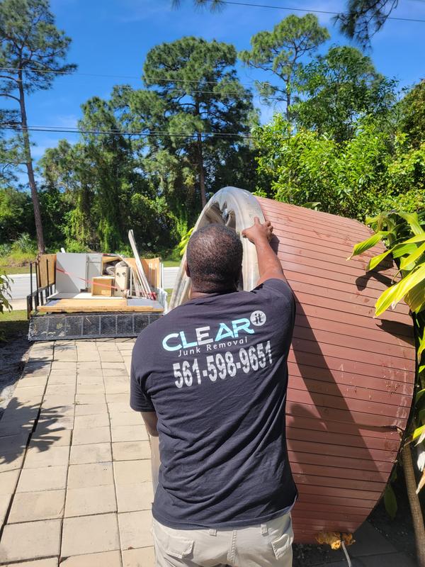 Clear It owner in a branded Clear It shirt loading debris beside a full trailer